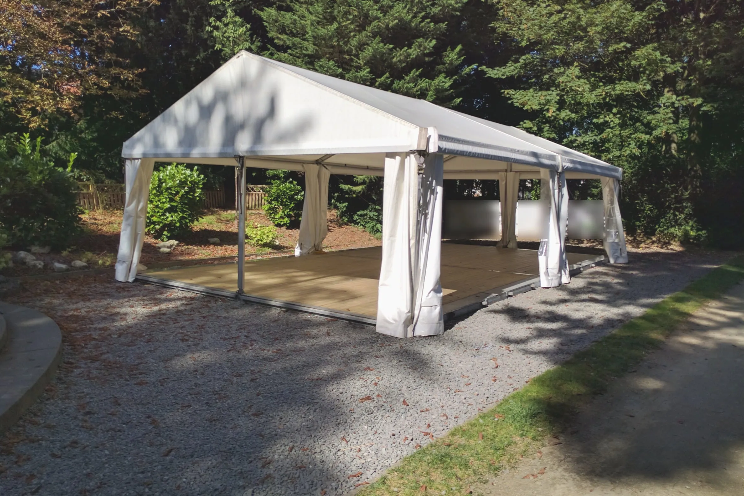 Chapiteau blanc de Chapiteaux en Fête monté sur un plancher, dans un jardin arboré