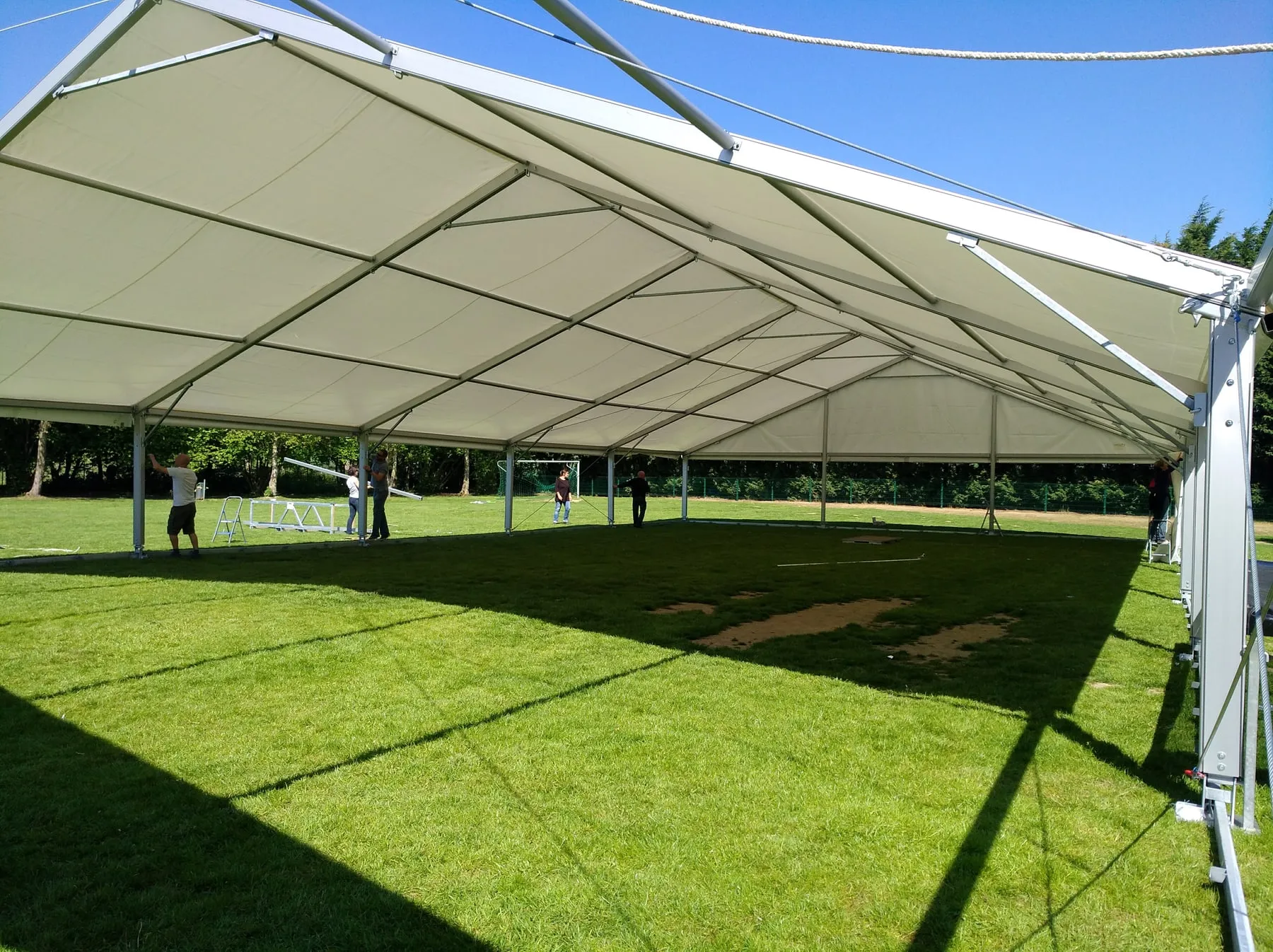 Grand chapiteau blanc en cours de montage sur une pelouse, sous un ciel bleu
