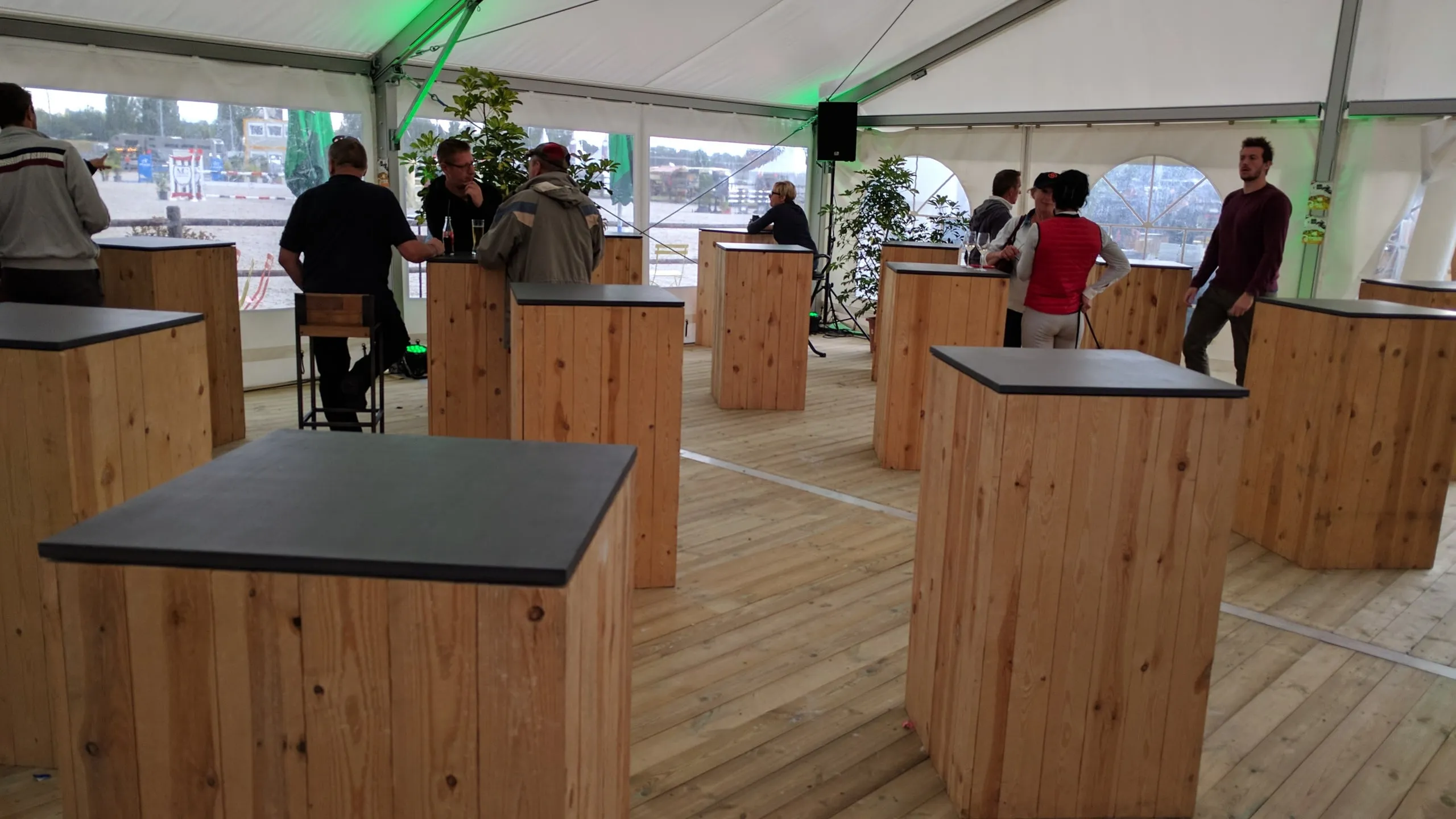 Mange-debout en bois sous un chapiteau, des invités autour